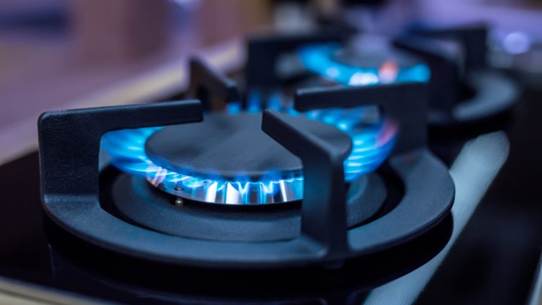 A gas cooking range is turned on, showing the blue flame sitting underneath the black metal stovetop.