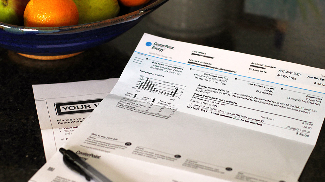 An electric utility bill sits on a kitchen countertop next to a bowl of fruit.