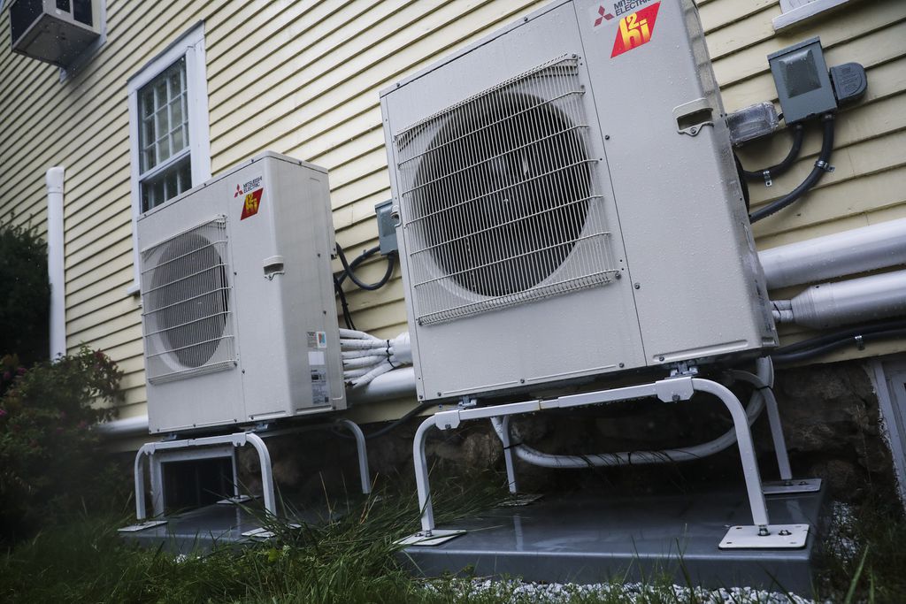 Grey heat pumps installed on the outside of a cream-colored Massachusetts house. 