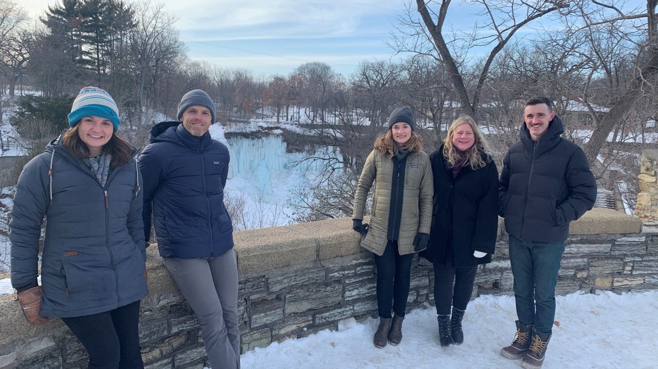 Fresh Energy's Clean Electricity team poses at a scenic overlook in front of the frozen Minnehaha Falls in south Minneapolis, Minnesota.