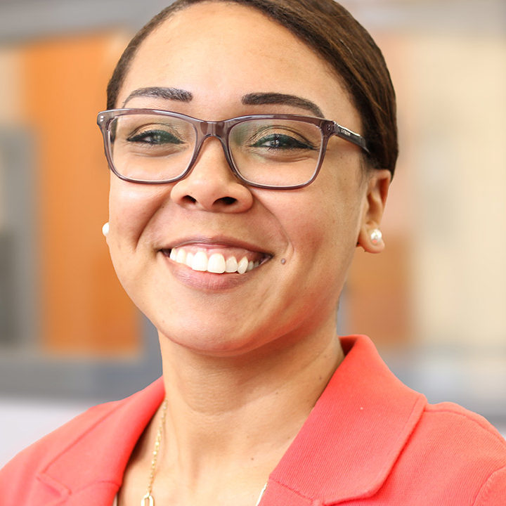 Fresh Energy's policy associate, energy access and equity, Mari Ojeda, smiles for the camera in a portrait. Mari is wearing a bright coral blazer and brown rimmed glasses, with her hair pulled back.