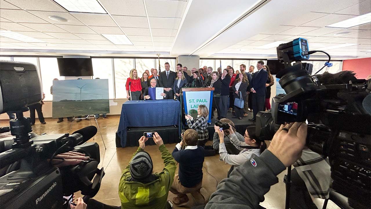 Governor Walz holding up recently signed 100% Clean Electricity law with leaders on the bill pictured behind.