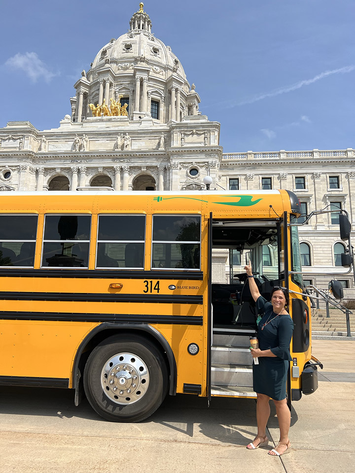 Electric school bus on display at the State Capitol with Brenda Cassellius standing next to it.