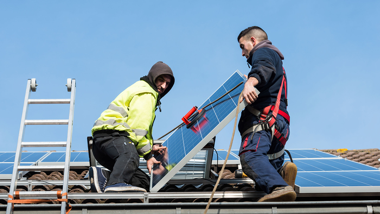 Two people installing a solar panel on the roof.