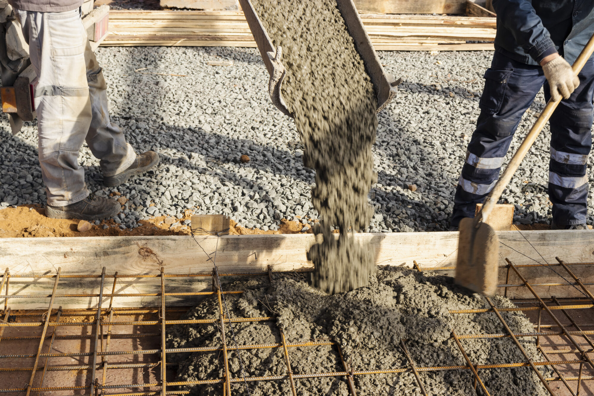 Pouring cement or concrete with a concrete mixer truck, construction site with a reinforced grillage foundation. Workers settle and level the concrete in the foundation