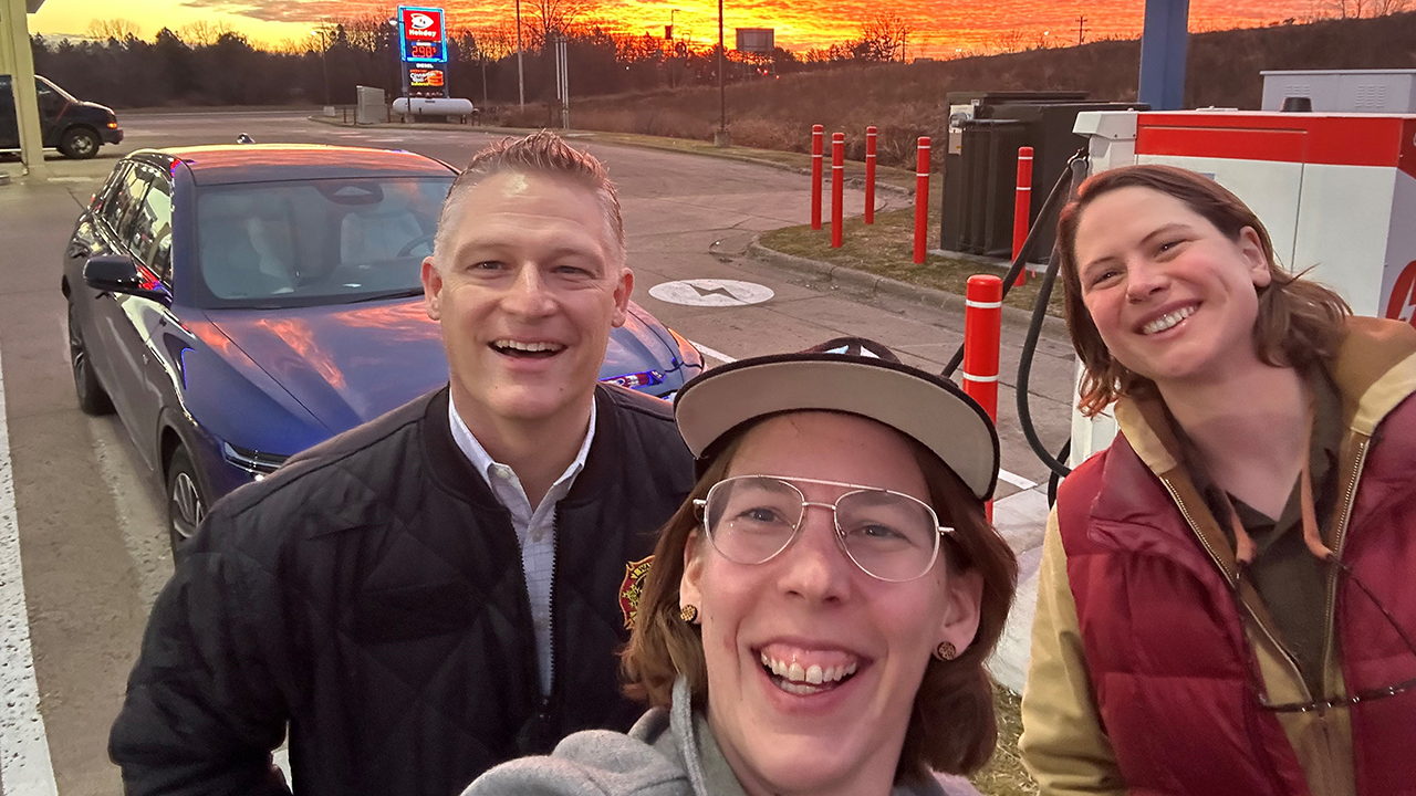 John, Brynn, and Anna smiling at an EV charging station at Sunrise. 