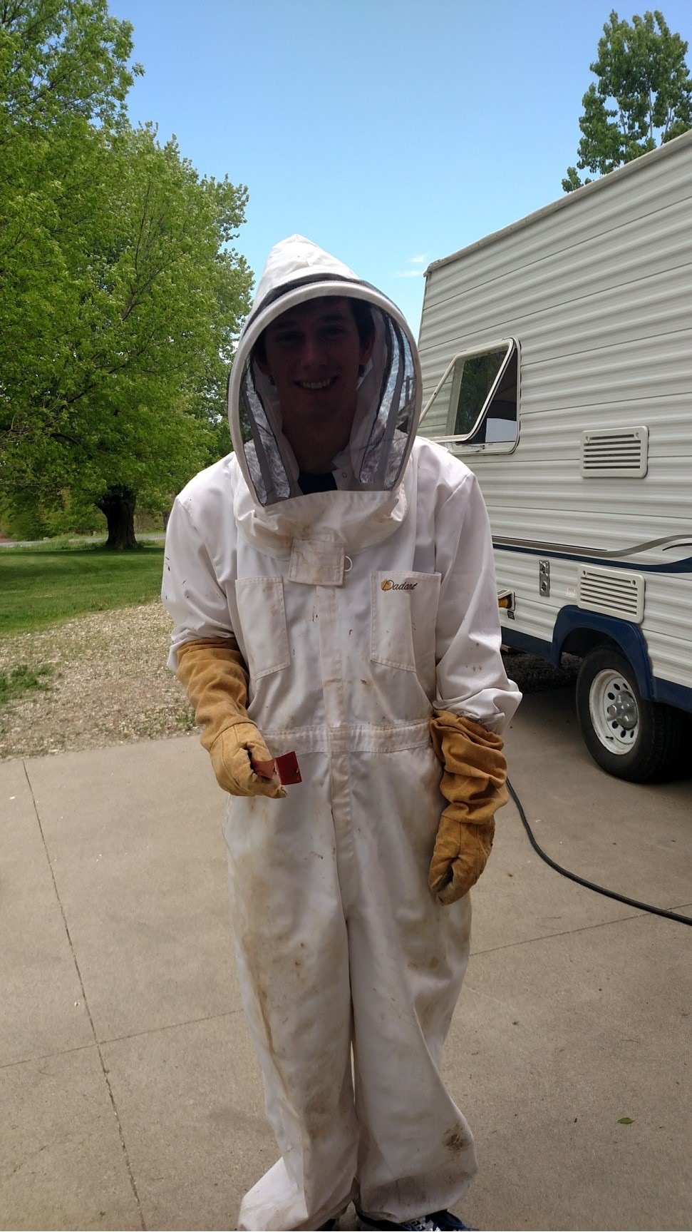 Nick wearing a bee keeping suit in front of camper on a sunny day. 