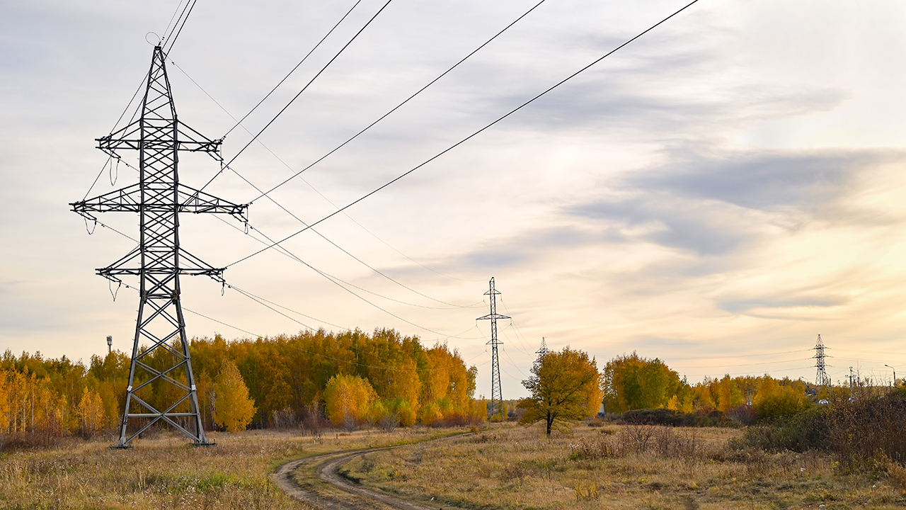 High-voltage power lines passing through a plowed field, on the background of a beautiful cloudy sky.