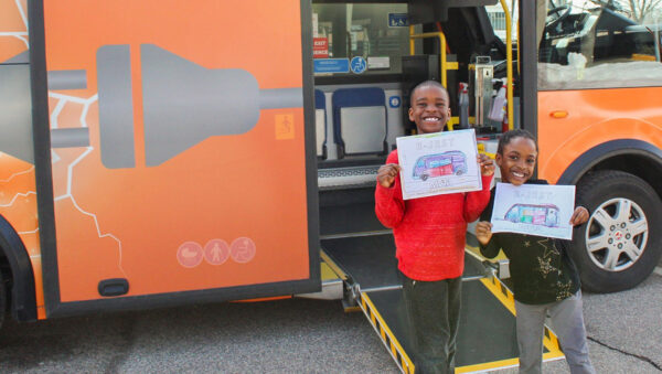 Two kids pose with drawings in front of MVTA's electric mini-bus.