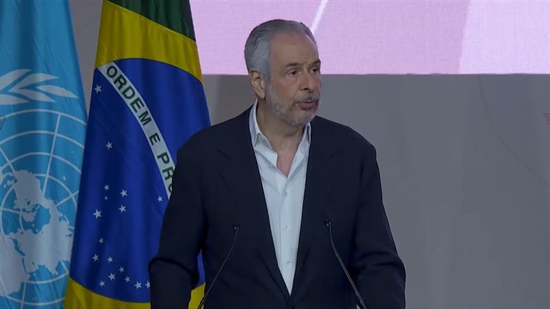 man speaks in front of Brazil and United Nations flag