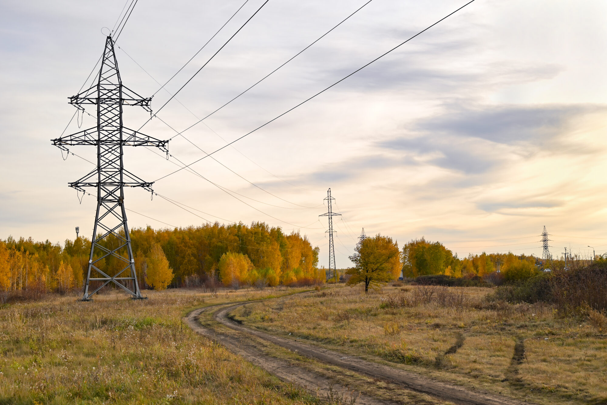 High-voltage power lines passing through a plowed field, on the background of a beautiful cloudy sky.